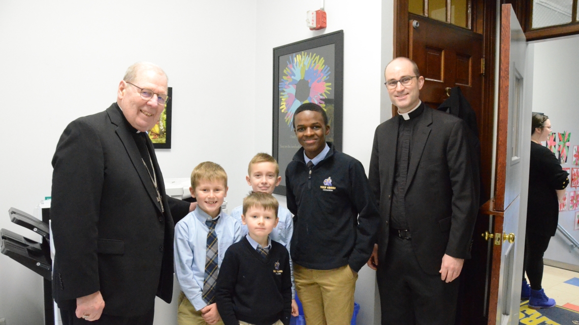 The bishop and a priest pose with three Catholic school students