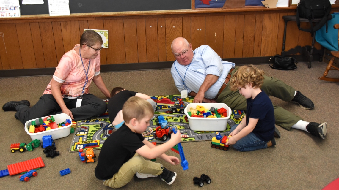 Foster grandparents playing on the floor with three preschoolers.