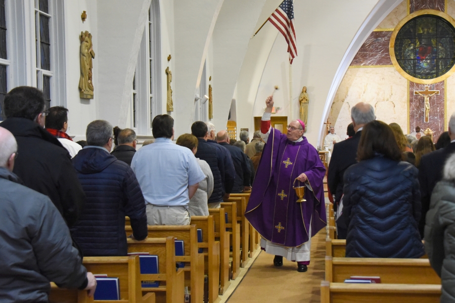 The bishop walks down the aisle sprinkling the walls with holy water.