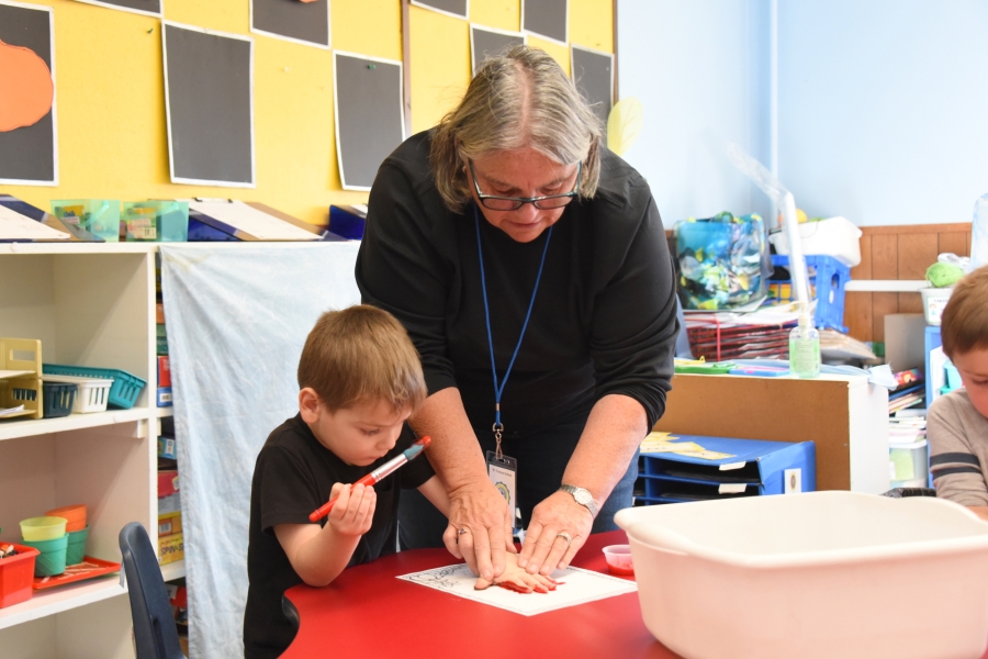A foster grandparent helps a preschooler make a handprint turkey.