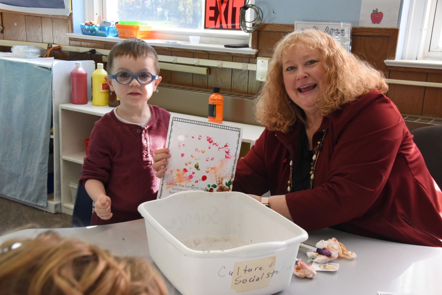 A foster grandparent and a preschooler display a handprint turkey.