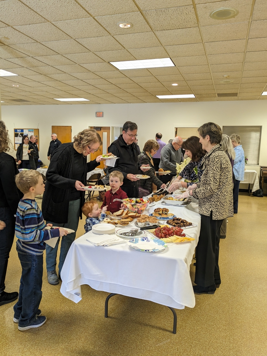 Group of people surrounding a table of food.