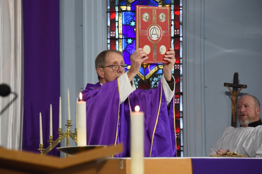 Father Dave Raymond holds up the Book of the Gospels.