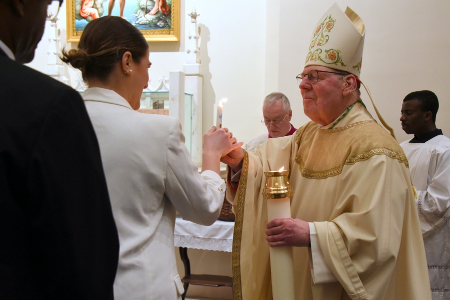 A godparent receives the baptismal candle from the bishop.