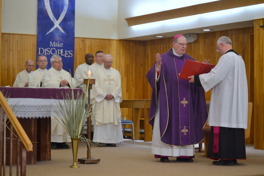 Bishop Deeley prays. There is a row of priests in the background.