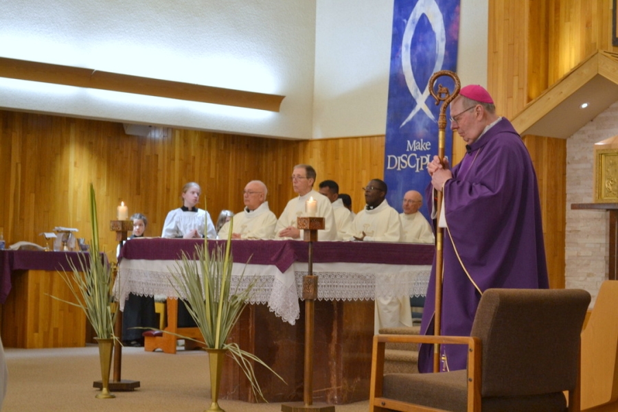 Bishop Deeley holds his staff while the Gospel is read.  Priests also stand in the sanctuary.