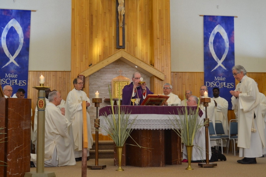 Bishop Deeley holds up the host during consecration with priests surrounding him.