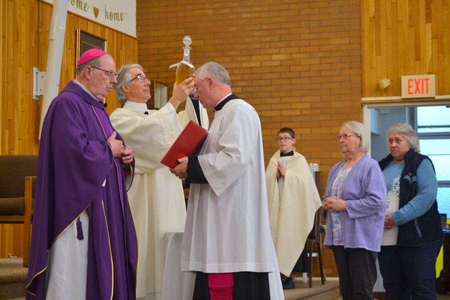 Deacon Carl Gallagher holds up a jar of oil next to Bishop Deeley and Msgr. Marc Caron.