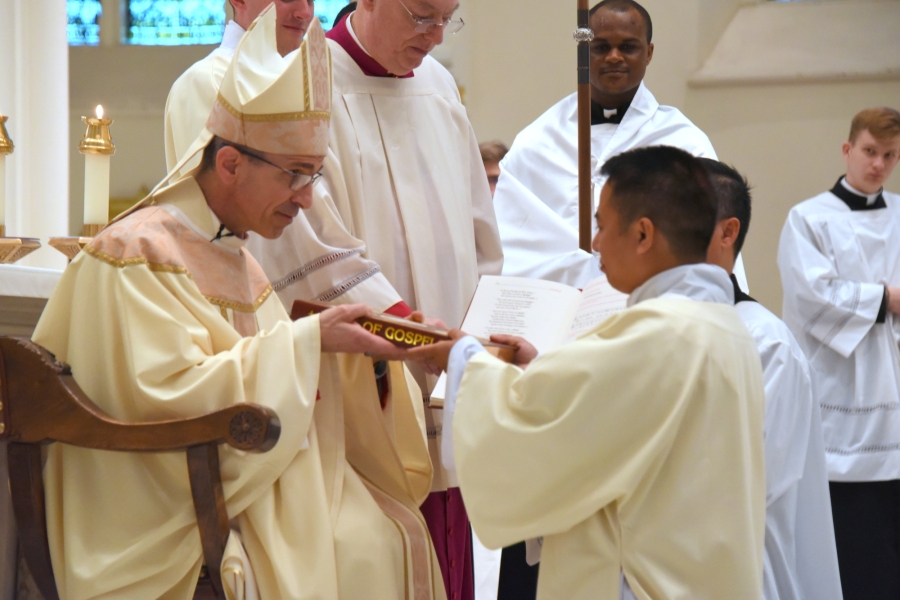 Bishop Ruggieri presents Tien Hoa Nugyen with the Book of the Gospels.