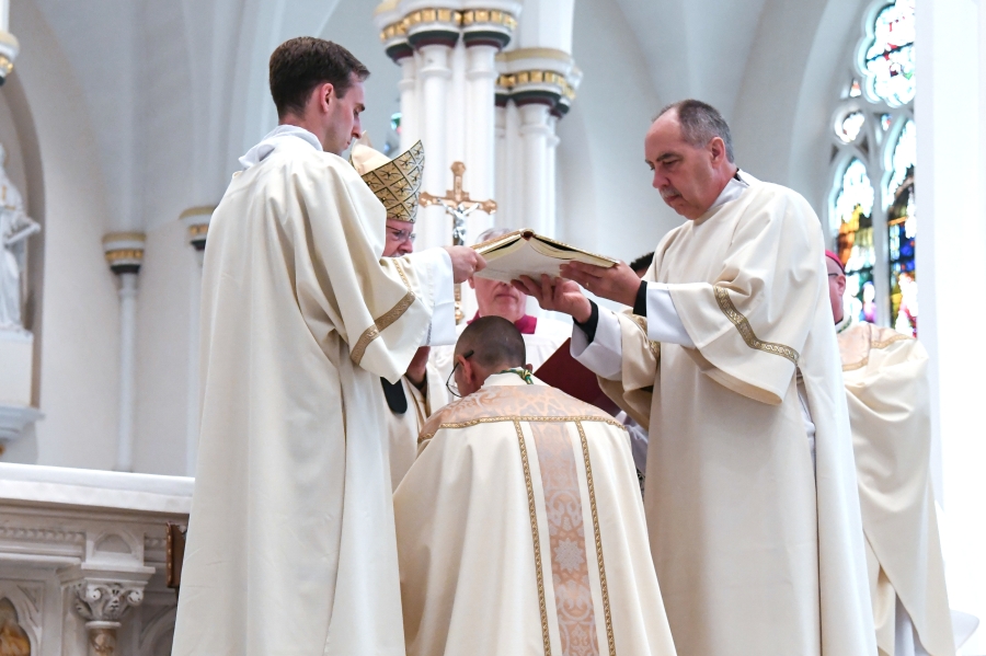 Deacons Matthew Valles and Timothy Dougherty hold the Book of the Gospels over Bishop Ruggieri's head.