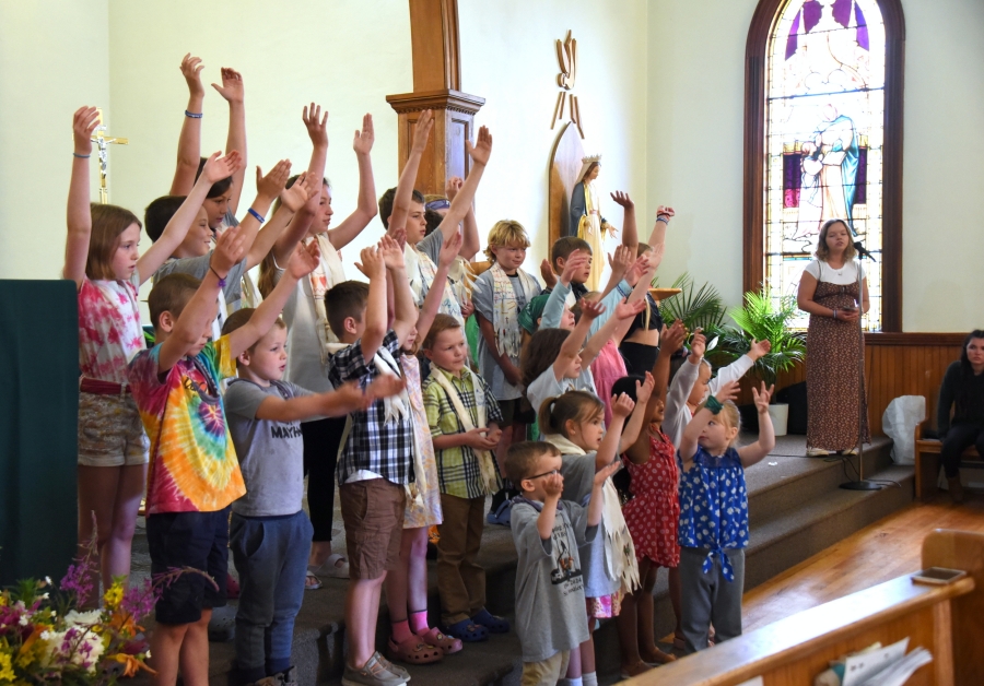 Children with arms raised as they sing a hymn in church.