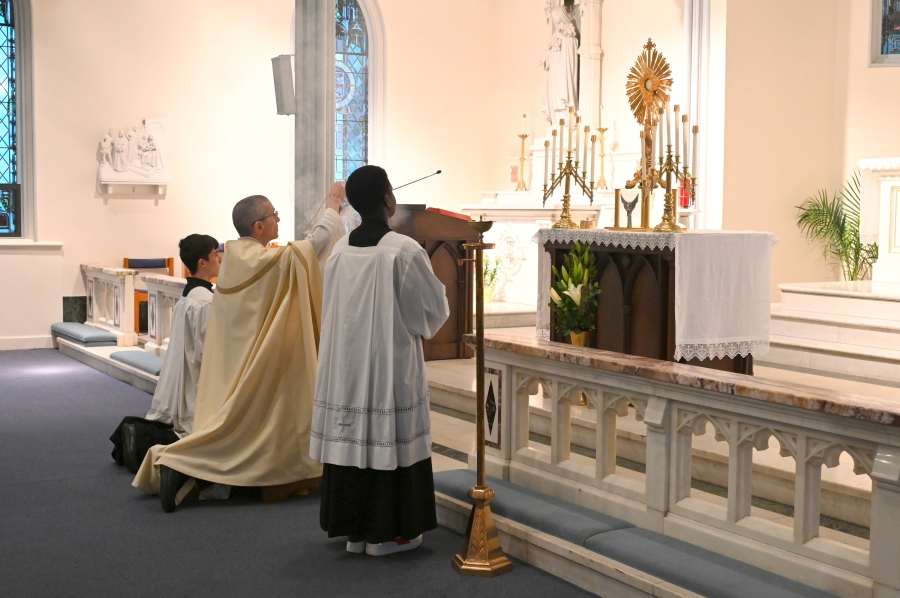 Bishop kneels before the altar with the monstrance on it, incensing it.