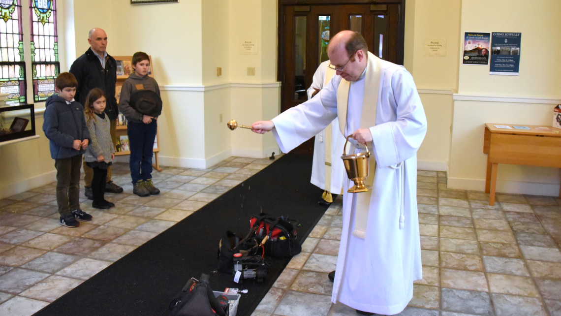 Father Kevin Upham sprinkles tools with holy water.