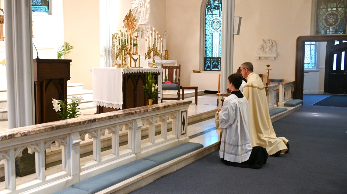Bishop Ruggieri and altar servers kneel before the altar and the Blessed Sacrament.