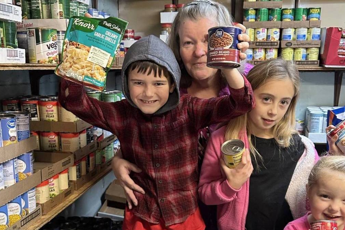 Children and a woman holding up cans of food at the Woodland Food Pantry.