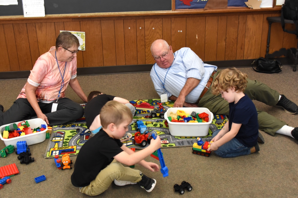 Foster grandparents playing on the floor with three preschoolers.