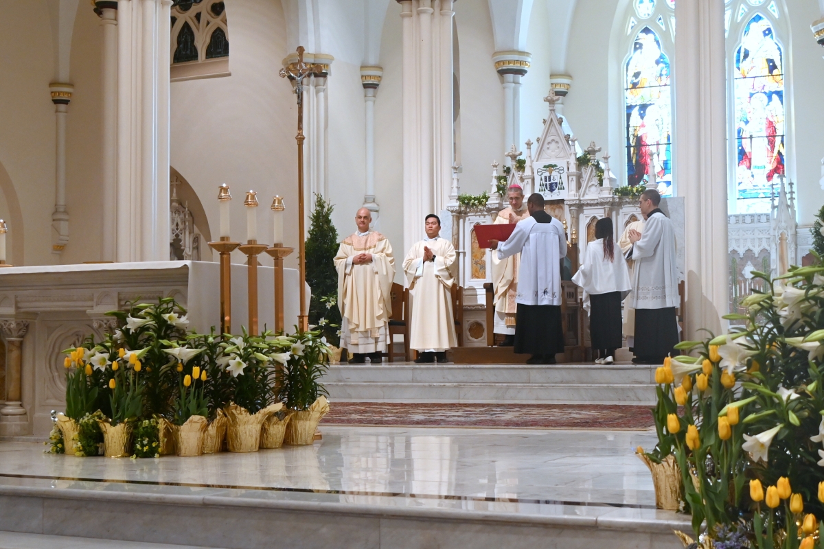 Bishop Ruggieri, Father Seamus Griesbach, altar servers, with flowers in the foreground.