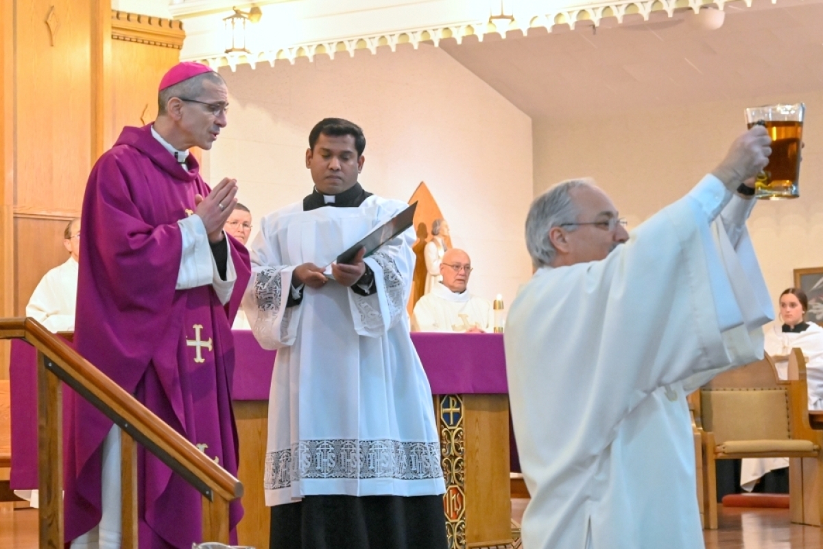 Deacon Rodney Dechaine holds up oil with Bishop James Ruggieri behind him.